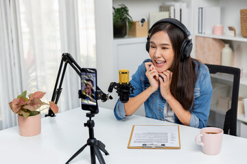 Host channel Asian influencer talking in broadcast wearing headsets on social media live on smartphone recording online, greeting listeners with coaching life or business at modern studio. Stratagem.