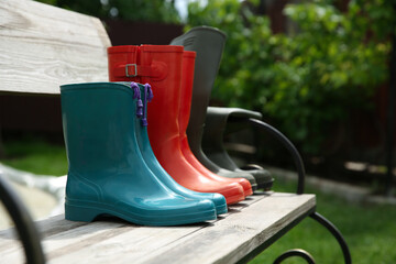 Three pairs of rubber boots on wooden bench outdoors