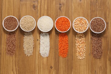 Sticker - Different types of cereals and legumes in bowls on wooden table, flat lay