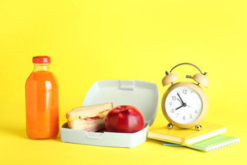 Wall Mural - Lunch box with snacks, bottle of juice, alarm clock and books on yellow background