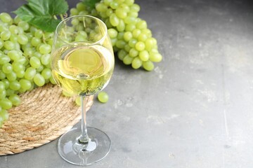 Fresh ripe grapes and glass of wine on grey table. Space for text