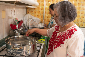 Women dressed in traditional Mexican clothing preparing the ground beef filling needed to prepare traditional chiles en nogada in a traditional kitchen.