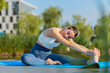© Andrii Iemelianenko - Flexible Caucasian young woman in sportswear doing stretching exercising on yoga mat near pond in park. Adult sportswoman girl bending forward represents healthy lifestyle. Athletic sporty female.