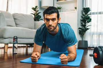 Wall Mural - Athletic and sporty man doing plank on fitness mat during home body workout exercise session for fit physique and healthy sport lifestyle at home. Gaiety home exercise workout training.