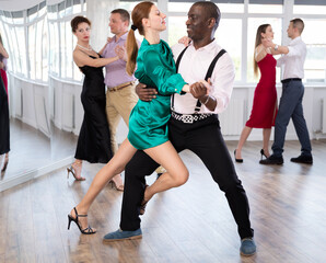 Wall Mural - Woman paired with African American man practices movements of Latin tango dance and trains to perform movements during lesson in choreography studio.