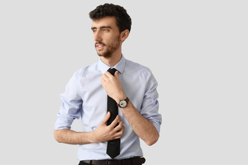 Poster - Young businessman fixing necktie on light background