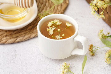 Cup of linden tea and bowl with honey on white table