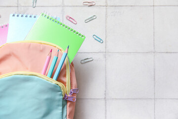 Wall Mural - Colorful school backpack with notebooks, pencils and paper clips on white tile background