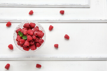 Glass bowl with fresh raspberry on light wooden background