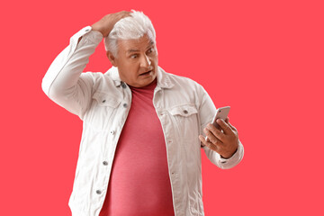 Wall Mural - Shocked senior man using mobile phone on red background