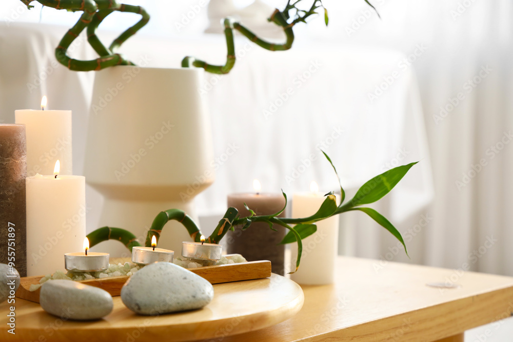 Burning candles with stones and bamboo on table in spa salon, closeup