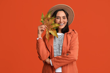 Wall Mural - Beautiful young woman with autumn leaves on red background