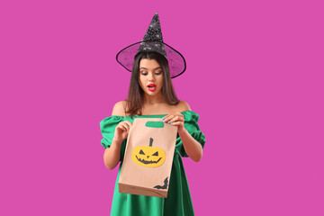 Wall Mural - Shocked young woman dressed for Halloween as witch with gift bag on purple background