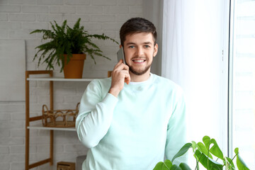 Wall Mural - Young bearded man talking by mobile phone at home