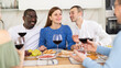 © JackF - Casual evening where multiethnic group of cheerful carefree adult friends sharing wine, dining together, and chatting in cozy home kitchen