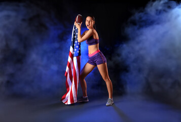 Poster - Sporty young woman with rugby ball and USA flag on dark background