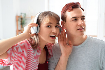 Poster - Young man with hearing aid and his girlfriend in headphones at home, closeup