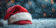 © Vertigo Images - A red Santa hat with white fur trim sits on the snow with a festive bokeh background.