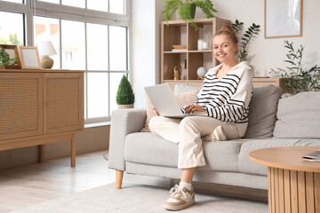 Sticker - Young woman using modern laptop on sofa at home