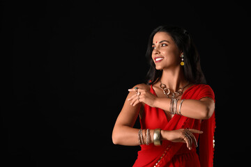 Wall Mural - Beautiful young happy Indian woman in traditional sari dancing on black background. Divaly celebration