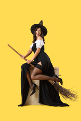 Wall Mural - Attractive young witch with broom on yellow background