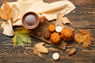 Wall Mural - Composition with candles in shape of pumpkins, cup of tea and fallen leaves on wooden background