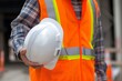 © srenhouse - Construction worker wearing safety vest and holding helmet