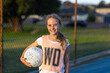© Austockphoto - schoolgirl standing with netball under her arm and smiling at camera