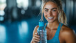 © Joelmir - femaleathlete in workout attire, smiling and holding a shaker bottle by her side filled with water after a gym session