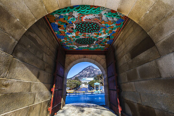 Jongno-gu, Seoul, South Korea - January 7, 2021: Low angle view of Sinmumun Gate of Gyeongbokgung Palace with daragon mural on ceiling against Blue House and Bugaksan Mountain in winter