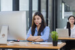 © SOMKID - Young asian businesswoman with headset using desktop computer for customer support and online working in office, Call center helping for customers online concept.