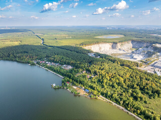 Big lake with green shores in bright sun light and city on horizon, aerial landscape. Recreation concept. Aerial view