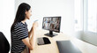 © NAMPIX - Young woman in casual clothes sitting at her desk at home, attending an online conference, drinking coffee and looking at the computer screen