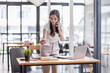 © David - Smiling asian female hold cell at ear talk look at laptop screen. Busy young asian lady advisor lawyer give phone consultation from workplace discuss electronic document details
