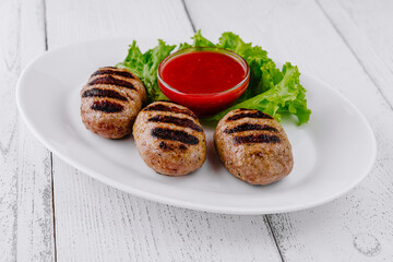 Three grilled meatballs with red sauce on white plate resting on white table