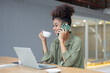 © SOMKID - African American young woman using smartphone with laptop computer.