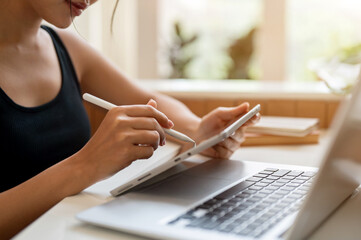 Wall Mural - A cropped side view image of a woman working remotely from a coffee shop, using her digital tablet.