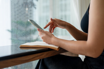 Wall Mural - A cropped image of an Asian woman using her smartphone at a table in a coffee shop.