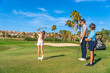 © unai - Girl swinging golf next to her family in a course