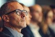 © Salander Studio - a middle aged man in glasses sitting in the audience listening to a speech - corporate conference setting
