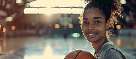 An indoor court setting featuring a smiling African American woman portrayed as a basketball player holding a ball gazing at the camera with available copy space image