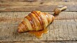 © arri - A Golden Croissant Drizzled with Honey on Wooden Surface