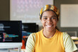 © Mediaphotos - Front view portrait of Black young woman smiling at camera while sitting at desk and studying IT at school, copy space