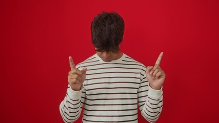 Sticker - Young hispanic man wearing stripes t shirt standing pointing up looking sad and unhappy, upset and indicating direction with finger, depressed over isolated red background