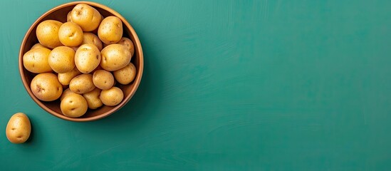 Poster - Top view of a bowl filled with fresh raw potatoes on a green background featuring copy space image