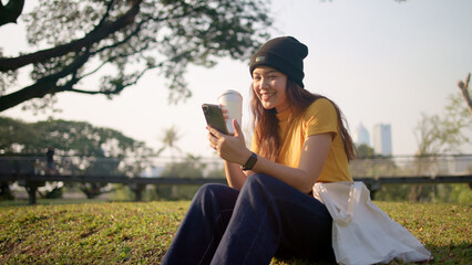 Gen Z eco go green woman asia sit happy relax at tree public park city life enjoy typing mobile phone drink coffee bottle use reuse tote bag care save the earth planet net zero waste clean future hope