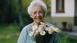 © halo - A happy elderly woman holding flowers and smiling while standing in the garden of a caring home, which is located outside.