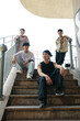 © DragonImages - Group of four friends standing on staircase and posing for photo outside under clear sky with relaxed and casual expressions engaging in friendly conversation