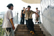 © DragonImages - Group of teenagers congregating on outdoor stairs near urban graffiti wall, interacting and casually posing. Scene capturing youth culture and camaraderie in casual setting