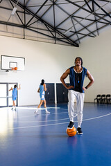 Wall Mural - Playing basketball, african american man while female players practicing in gym, copy space